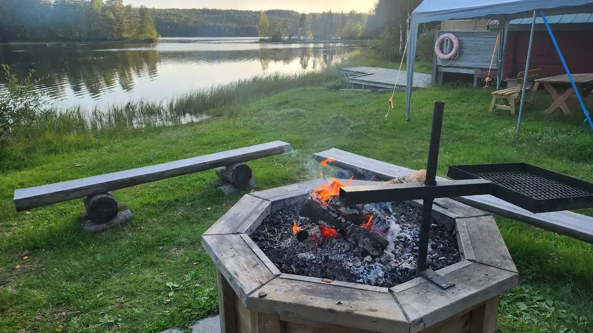En picknickplats med utomhusbord och bänkar vid en sjö i Lappland. Området omges av våtmarker och en rofylld naturmiljö.