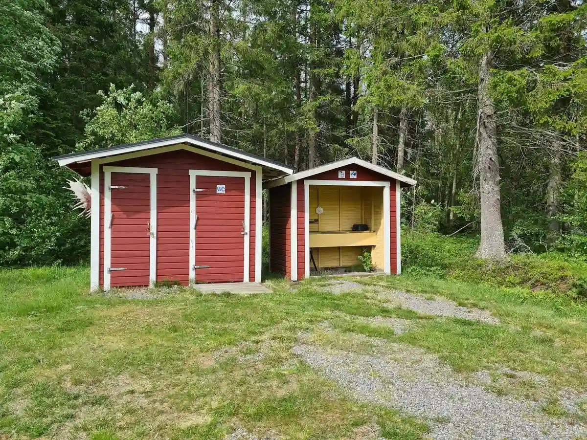 En rustik trästuga med en enkel dörr, omgiven av lummig skog och grönska, står på Storsands camping.