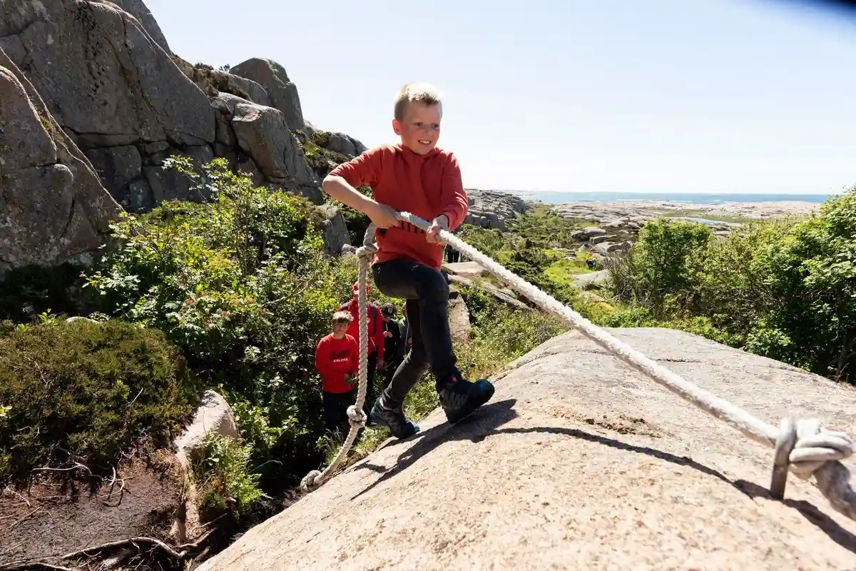 En äventyrlig scen vid Ramsvik Stugby & Camping med klippor och besökare som njuter av friluftsliv. Klättringsutrustning syns på de robusta bergssluttningarna, vilket bidrar till platsens lockelse för rekreation och utomhusäventyr.