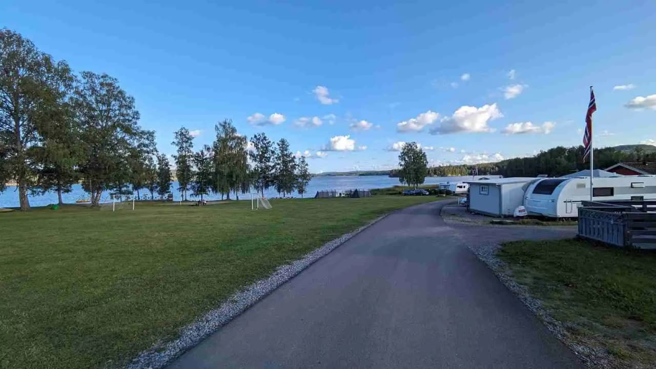 En campingplats vid en reservoar med husbilar och husvagnar omgivna av grönskande natur. Ett vattendrag syns i bakgrunden och platsen utstrålar en lugn och avslappnad atmosfär.