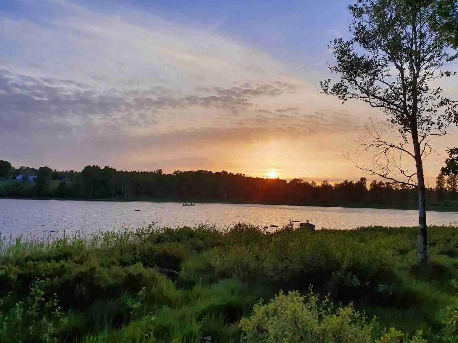 En naturskön bild av Kalvs familjecamping med stilla vatten som reflekterar himlen vid solnedgången, omgiven av en lugn och naturlig miljö.