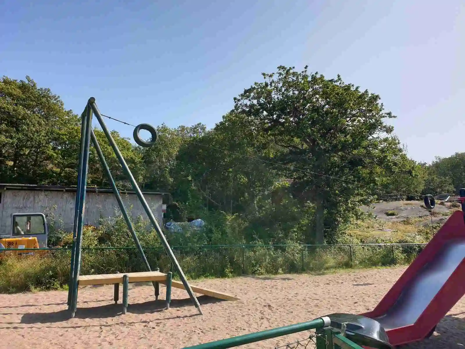 En lekplats på Marstrands familjecamping med gungor, rutschkana och andra lekredskap, omgiven av gröna träd och en öppen parkmiljö.