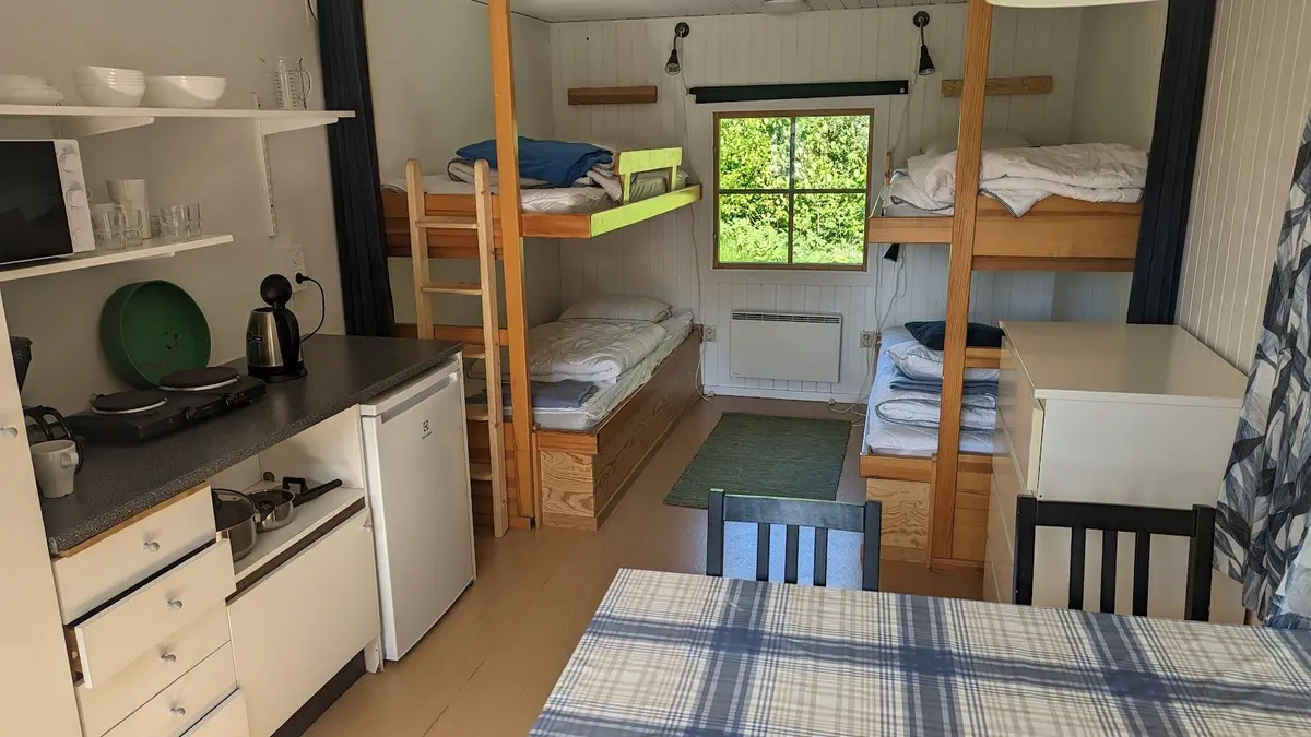 Alt-text: Bild av en enkel träinredd plats på Furulid, med våningssängar, trästolar och ett picknickbord i ljus träfinish.