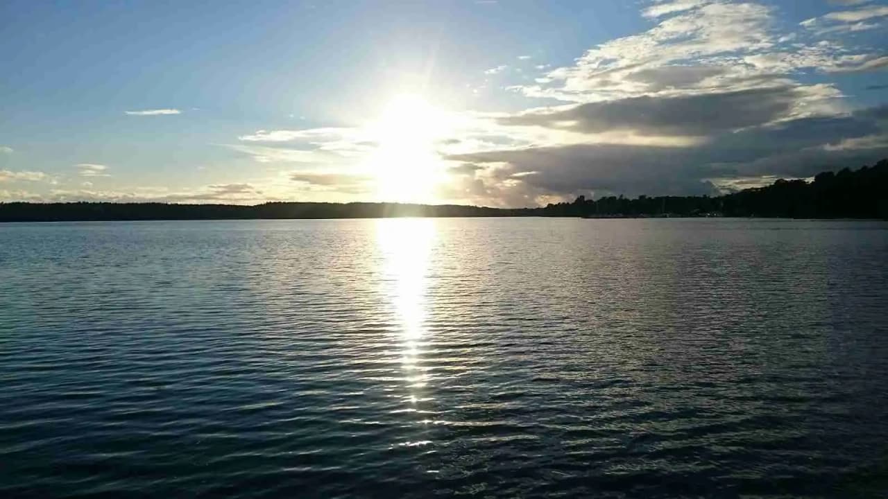 En vacker dag vid Ängby Camping med en blå himmel och vita moln som speglas i det intilliggande vattnet.