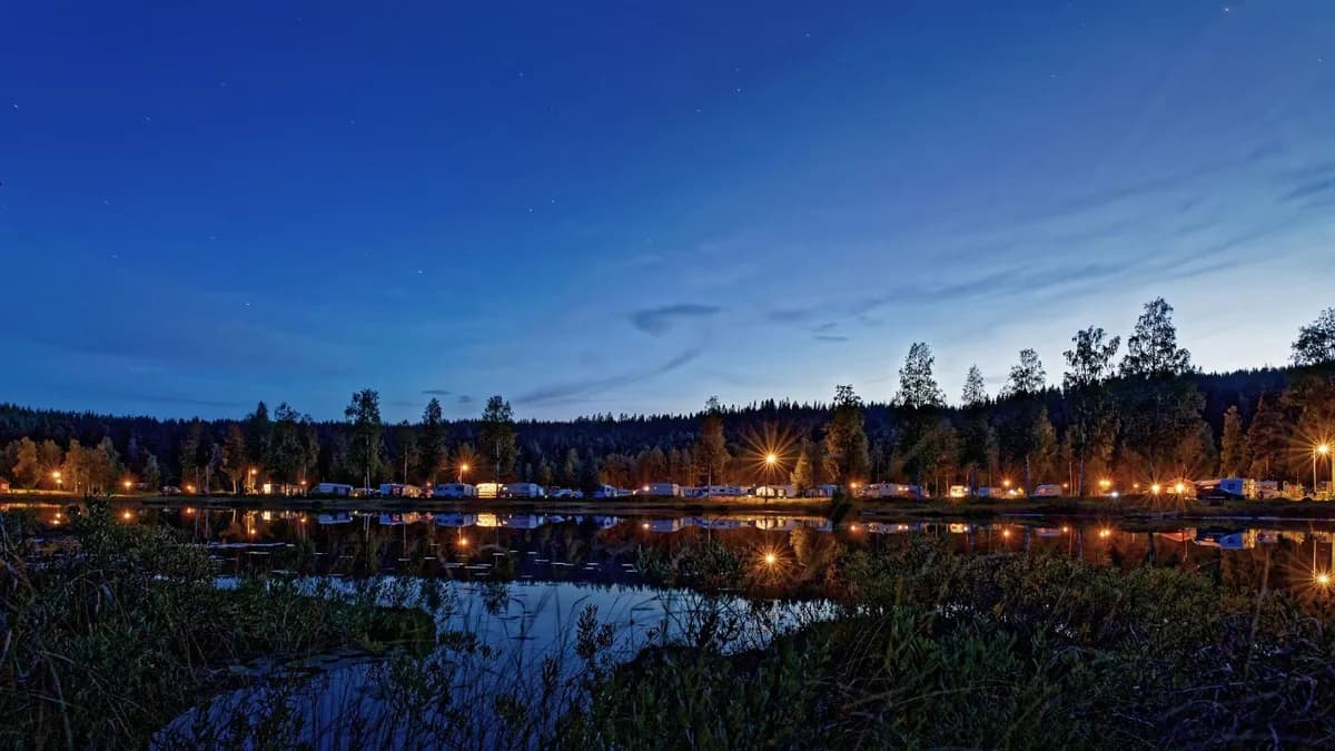 En fridfull sjö vid Malingsbo camping i skymningen, med speglingar av den blå kvällshimlen och omgivande landskap i vattnet.