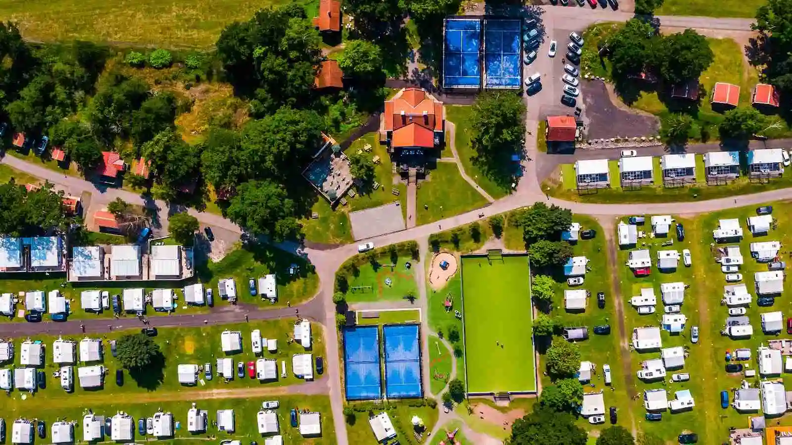 Flygbild över Västervik Resort som visar en stor campingplats med pool, parkerade fritidsfordon och omgivande grönska.