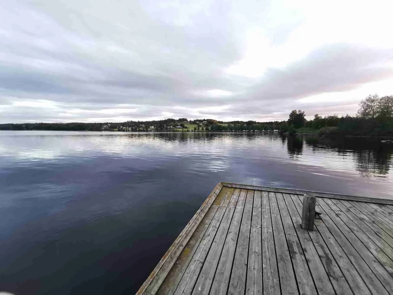 En klarblå himmel med fjäderlätta moln speglar sig i det lugna vattnet vid Hoverbergs camping, omgiven av vacker natur och vidsträckt horisont.
