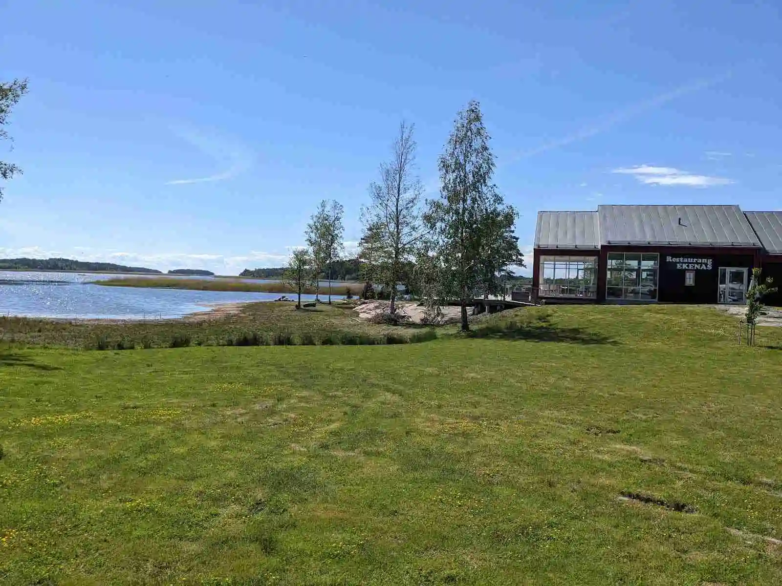 En pittoresk vy över Ekenäs gästhamn och camping med en lantlig känsla. Bilden visar en stuga omgiven av grönska vid en sjöstrand. Det öppna landskapet ger en känsla av ro och avkoppling i en lantlig miljö.