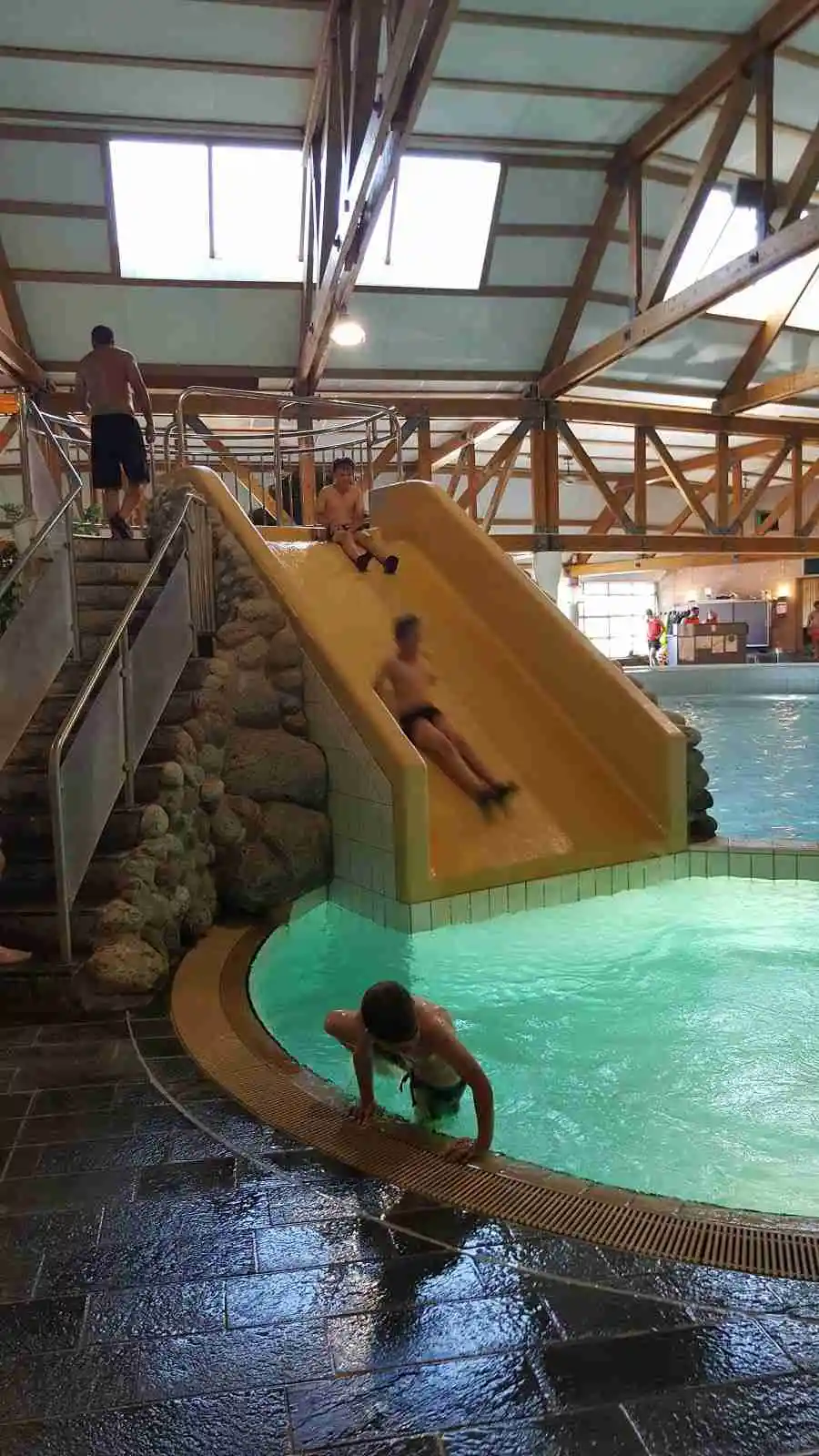 En livlig campingplats med en stor swimmingpool fylld med glada besökare som njuter av sol och bad. Miljön är inbjudande och perfekt för rekreation och semester.