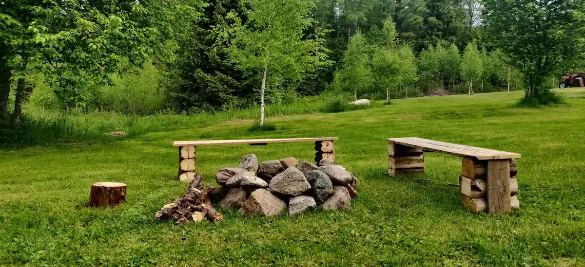 En träbänk och ett picknickbord står på en gräsmatta vid Solberg Hults Camping, omgivna av grönska och trädstammar i bakgrunden.