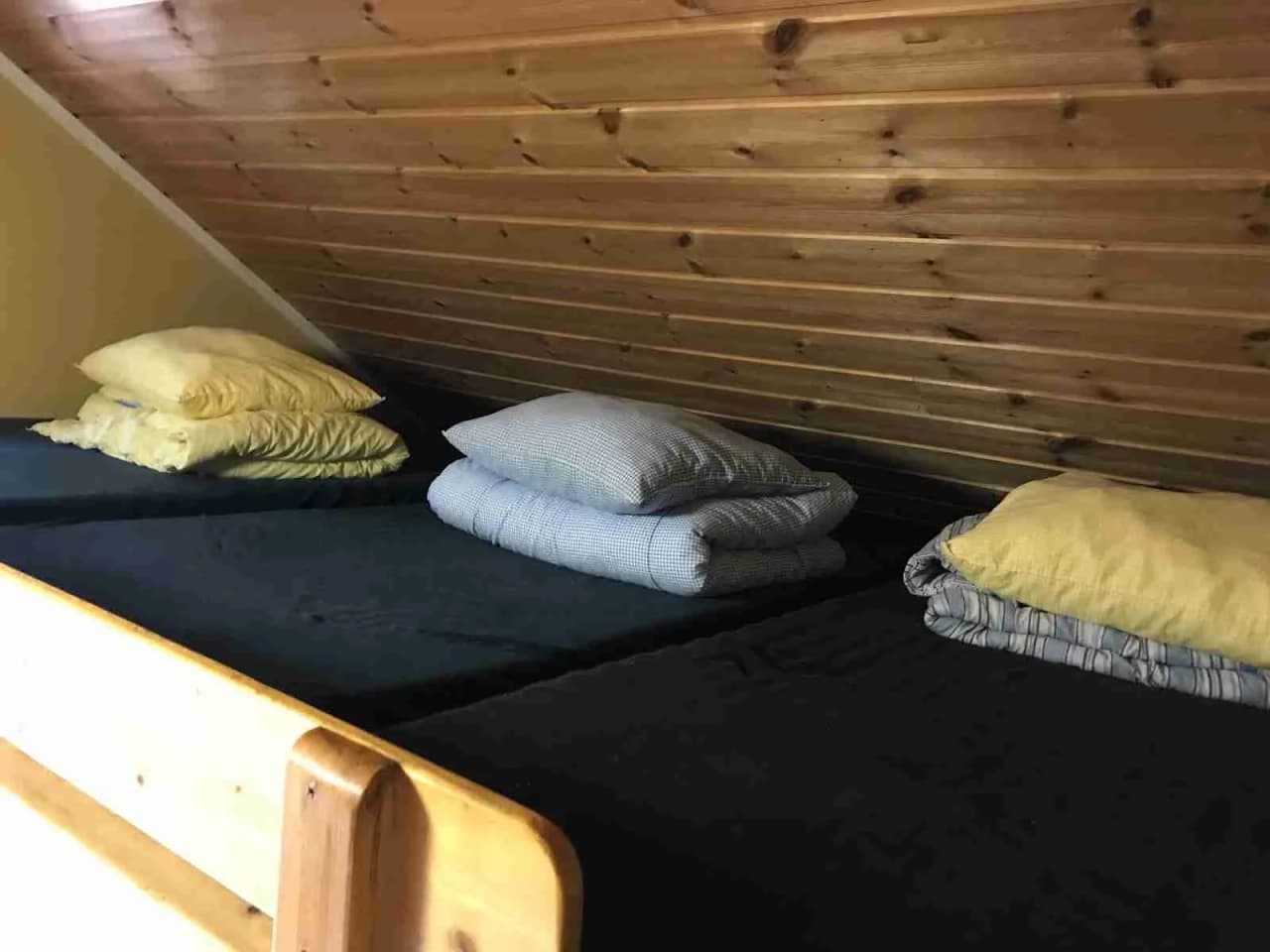 Bild av en träinredd sovrum vid Ängby Camping, med en dubbelsäng täckt av vita sängkläder, ett trägolv och enkel inredning.