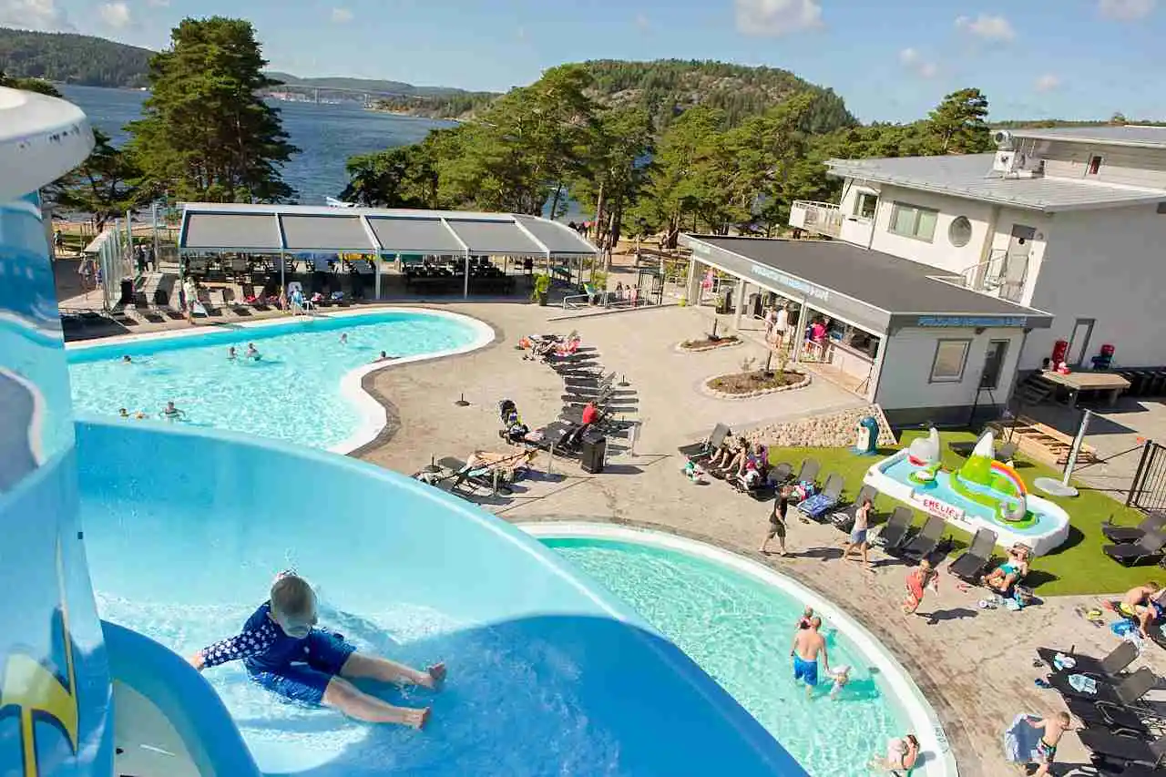 En livlig semestermiljö vid Hafsten Resort & Camping, med en pool omgiven av utomhusmöbler och parasoller, perfekt för avkoppling och rekreation.