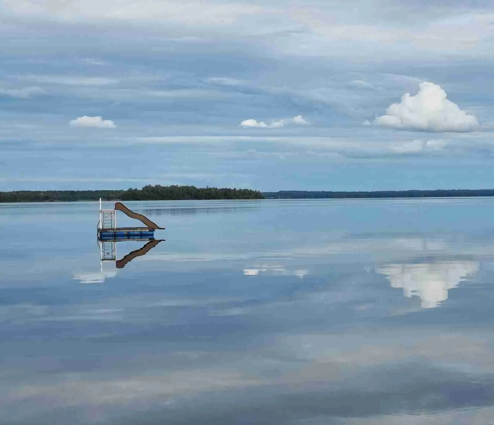 En klarblå himmel med vita cumulusmoln ovanför en bred vattenyta syns i dagsljus vid Löckna camping.