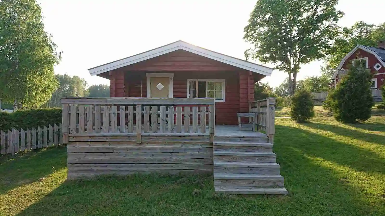 En trästuga med plåttak omgiven av grönska, som ger en hemtrevlig känsla på Charlottenberg camping & stugor - Haganäset.