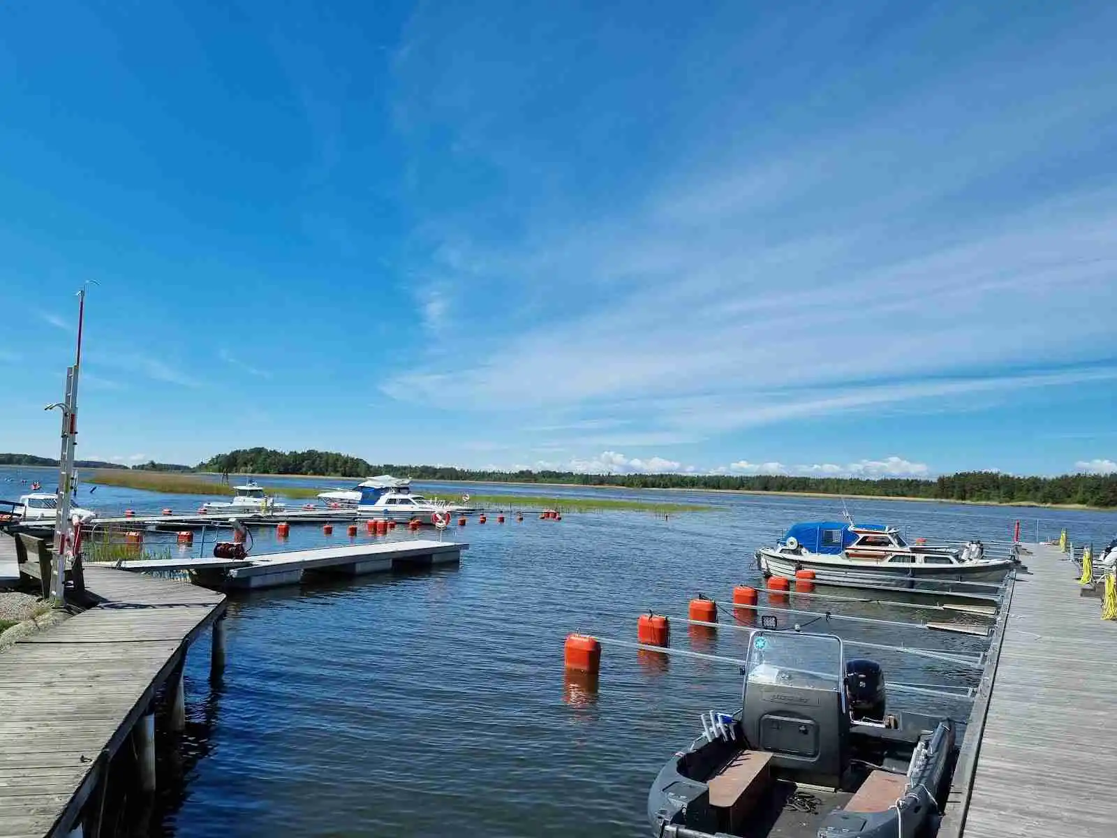 En solig dag vid Ekenäs gästhamn & camping, där flera båtar ligger förtöjda vid vattnet under en klarblå himmel med spridda vita moln.