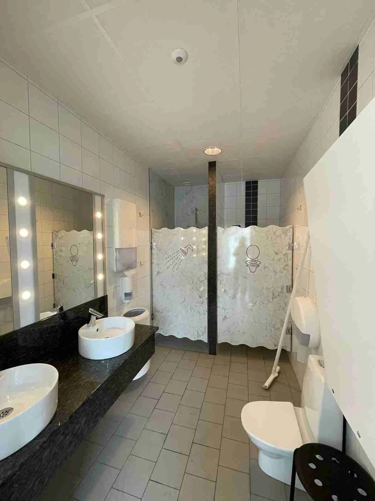 Ett modernt badrum på Hafsten Resort & Camping med stilren inredning. Här finns ett handfat monterat på en kaklad bänk, en spegel ovanför och eleganta ljusarmaturer. Badrummet har klinkergolv och kaklade väggar med en ljus och inbjudande känsla.