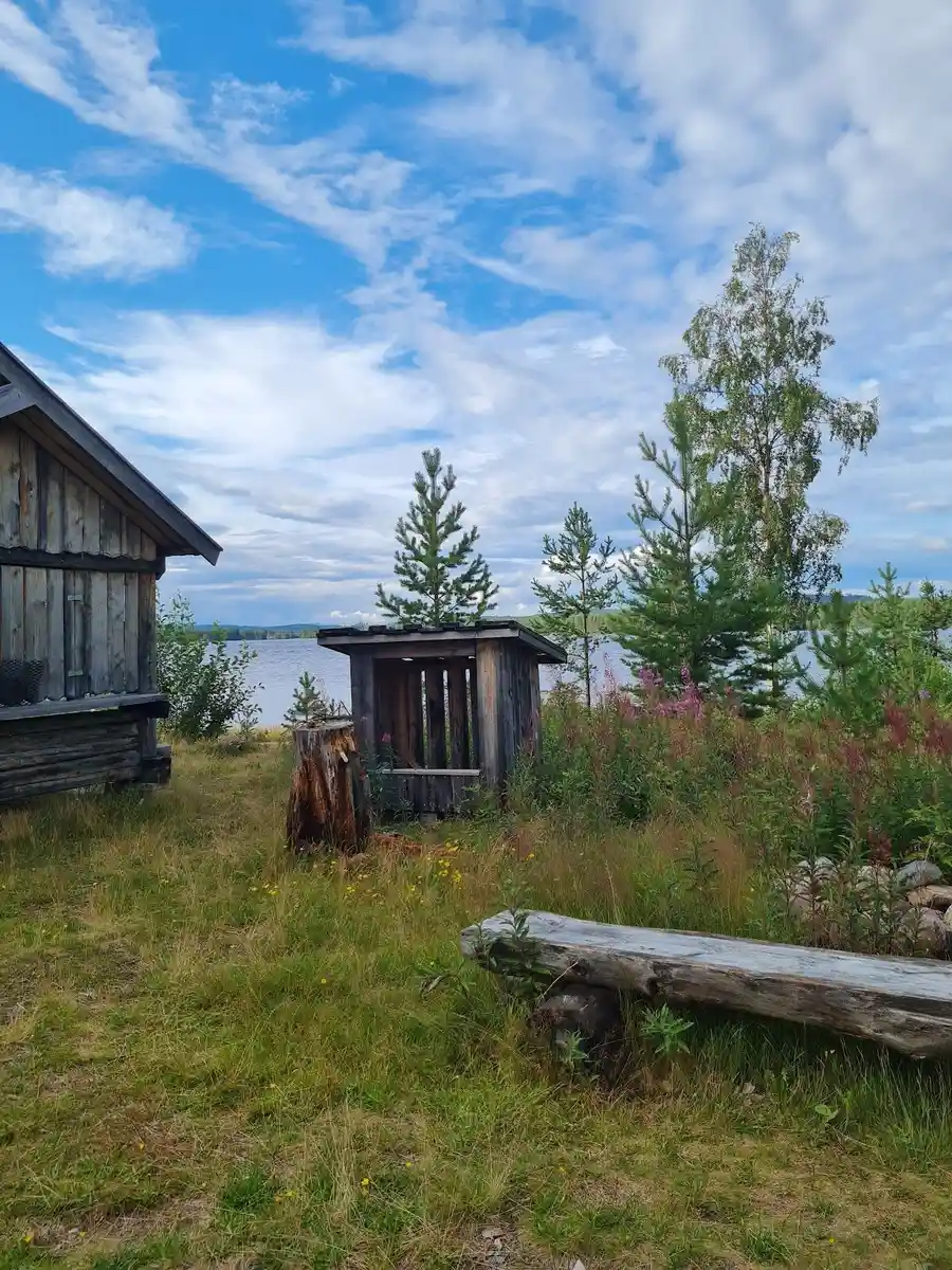 En grönskande campingplats med små, charmiga stugor och skjul omgivna av öppna ängar och ett vidsträckt landskap under en molnig himmel.
