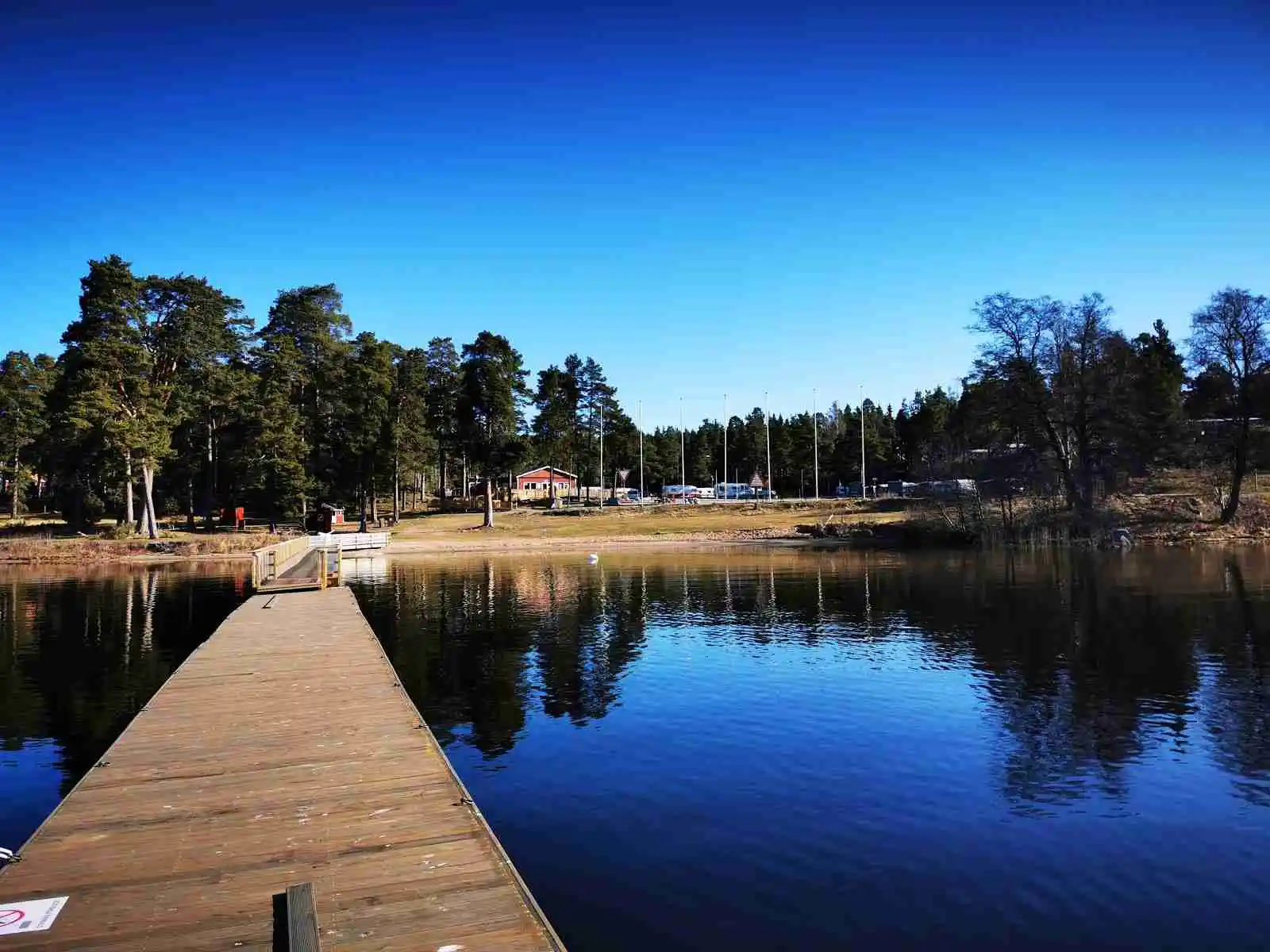 En lugn sjö vid Gävle camping Engesberg, omgiven av träd som speglas i det stilla vattnet.
