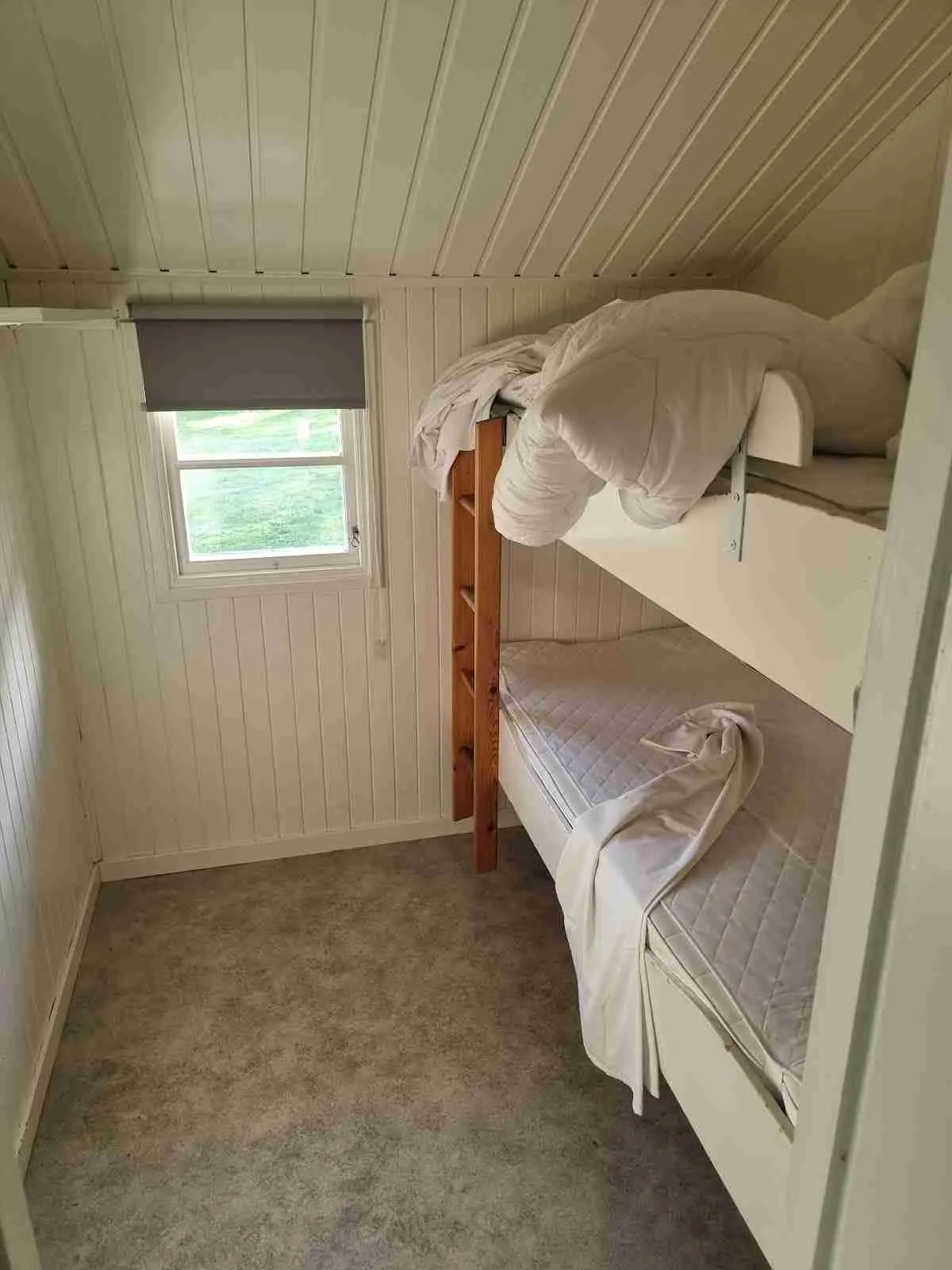 Ett inbjudande sovrum på Västervik Resort med trägolv och ljusa träväggar. Rummet har en dubbelsäng och en våningssäng, vilket ger plats för flera gäster. Inredningen är enkel och funktionell, med fokus på komfort.