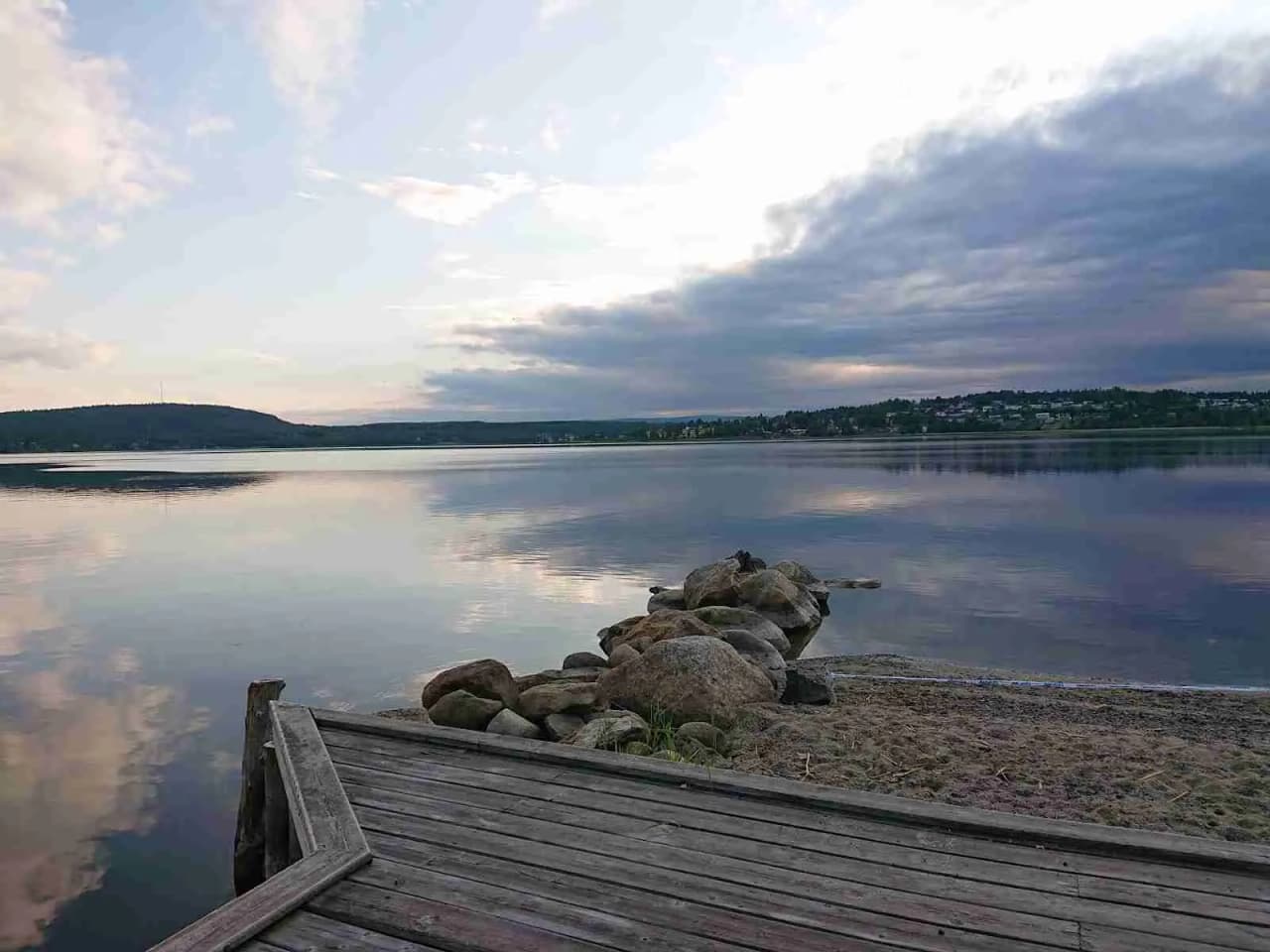 En vacker vy vid Solbacken med blå himmel och moln över horisonten. Vattnet i sjön speglar kvällens ljus och de omkringliggande kusterna.