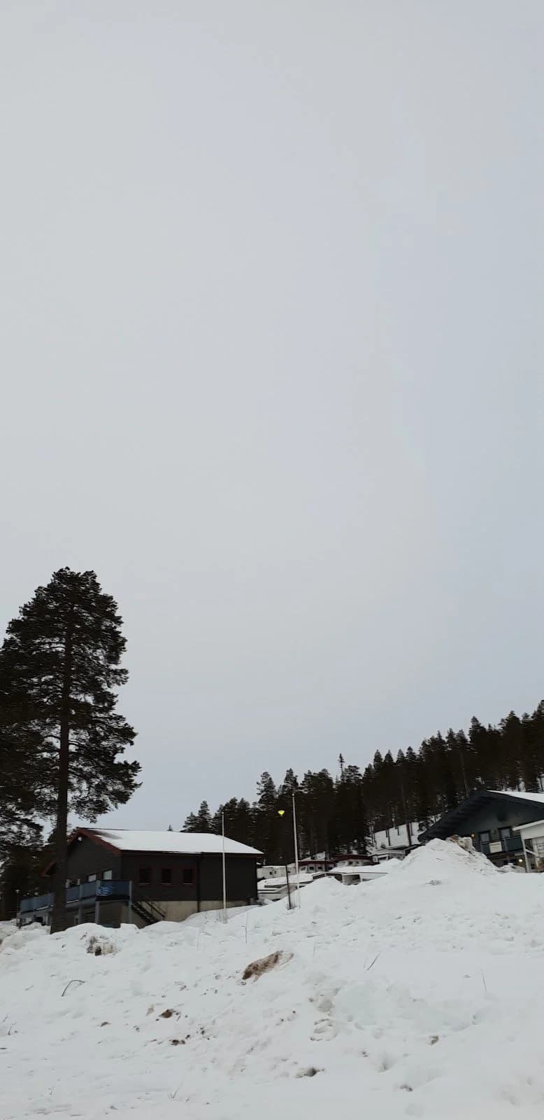 Snötäckt vinterlandskap vid Storklinta Skidcenter AB, med en backe och små stugor omgivna av lärkträd i ett gnistrande kallt klimat.