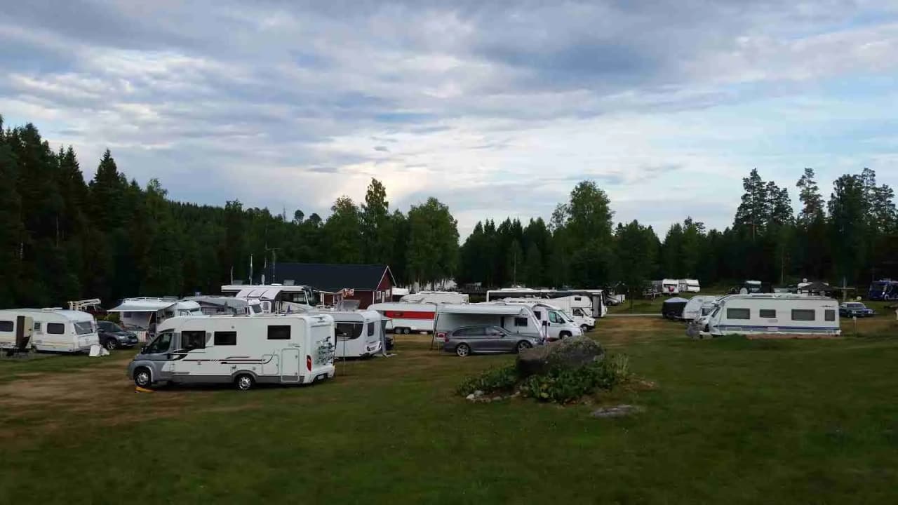 Bild av en campingplats i Sandviken med husvagnar och husbilar parkerade på området. Tält syns i bakgrunden och platsen omges av grönska, vilket ger en inbjudande atmosfär för camping och rekreation. 