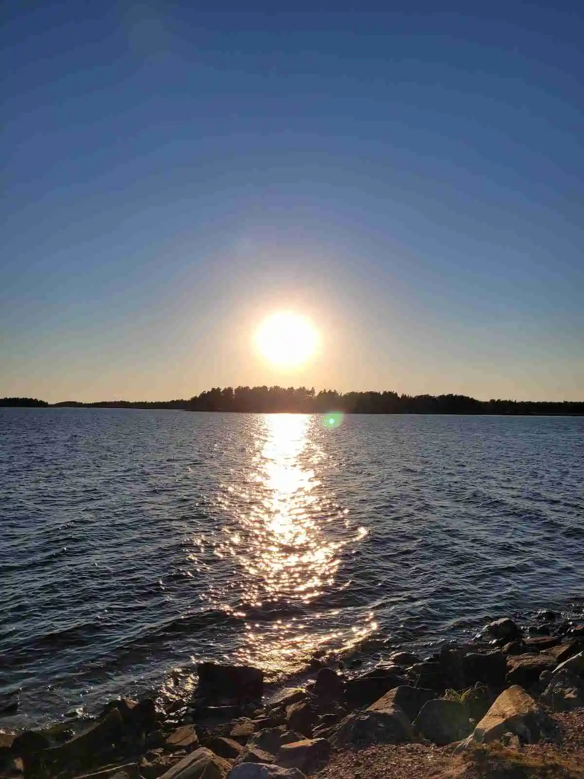 Bild på solnedgång över en vattenyta vid Malexander camping. Den strålande solen skapar gyllene reflektioner på vattnet, och horisonten är synlig i fjärran.
