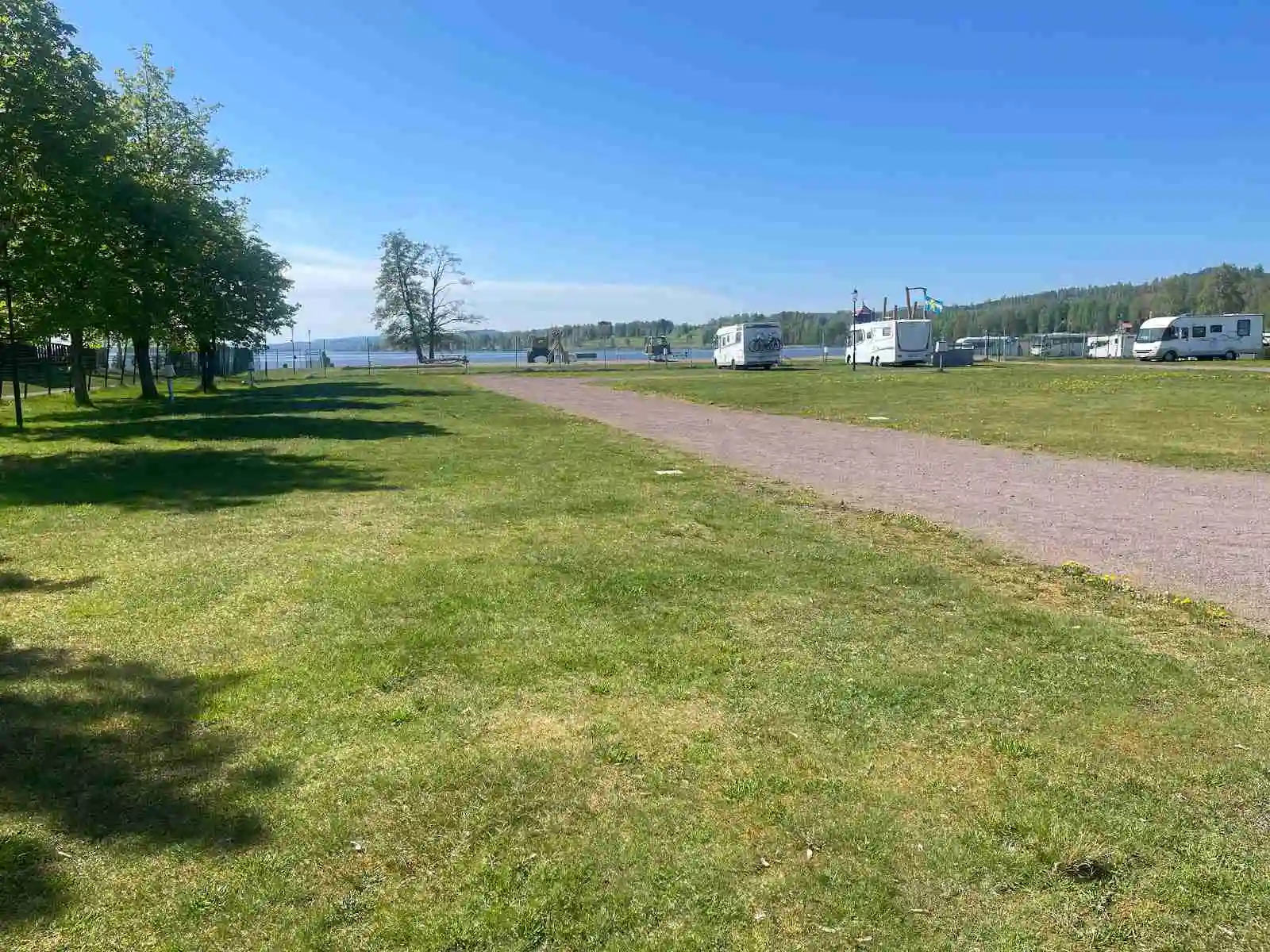 Bild av Sunne Camping och Sommarland: Ett öppet grönområde med välskött gräsmatta. Parkerade husbilar och husvagnar står i bakgrunden, vilket ger en känsla av ett livligt campingområde med gott om plats för rekreation och avkoppling.