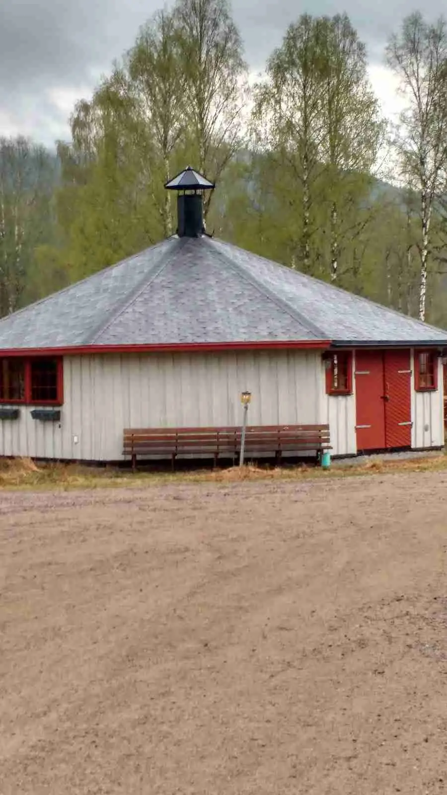 En trästuga med ett sluttande tak i skuggan, omgiven av gröna träd, vid Höljes camping.