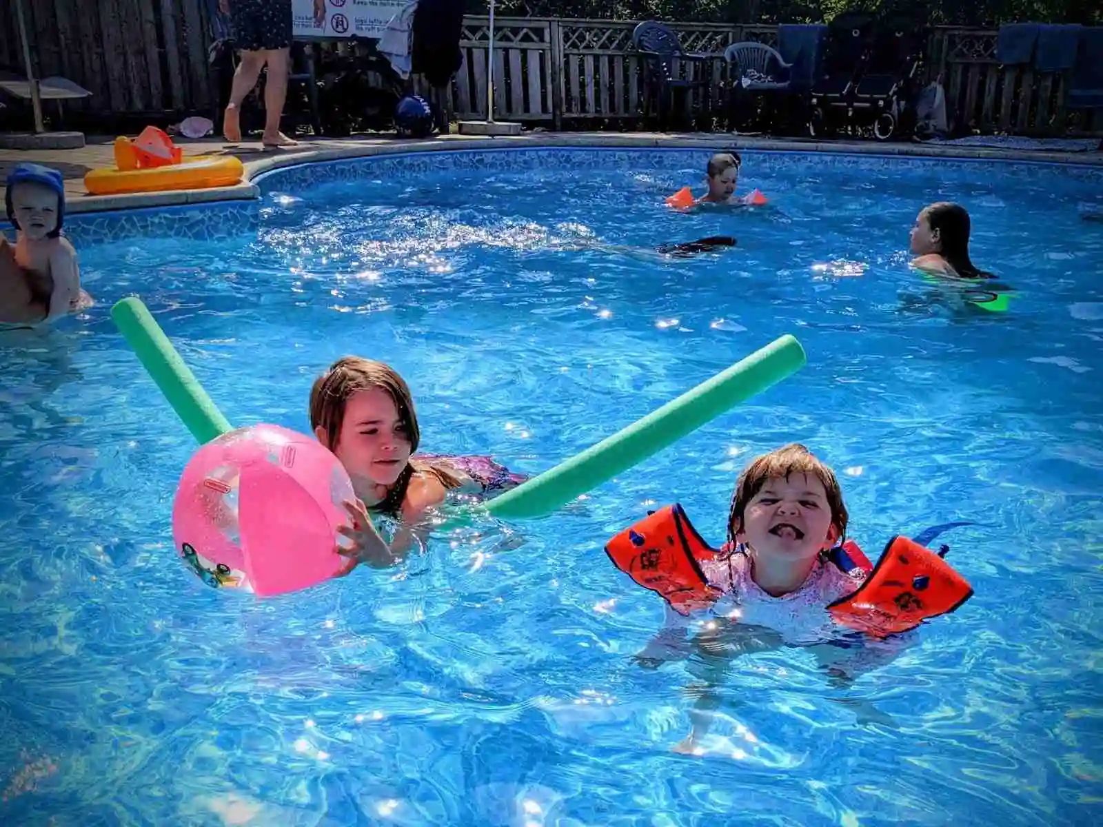 En somrig scen vid Grottbyns camping, där barn leker i en utomhuspool med färgglada uppblåsbara leksaker under en solig semester.