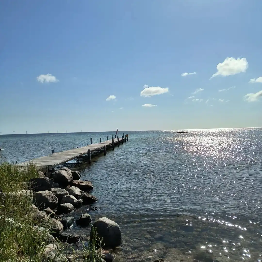 En utsikt över en brygga som sträcker sig ut i ett lugnt hav under en blå himmel med spridda vita moln.