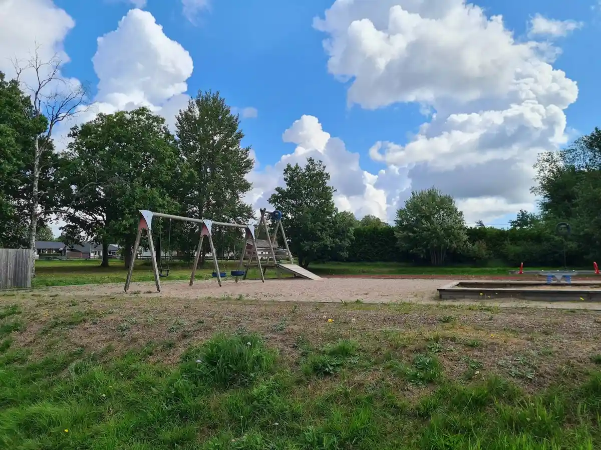 Bilden visar en öppen gräsyta vid Kosta bad och camping, omgiven av träd under en blå himmel med vita moln. Det är dagtid och platsen ger en känsla av lugn och natur.