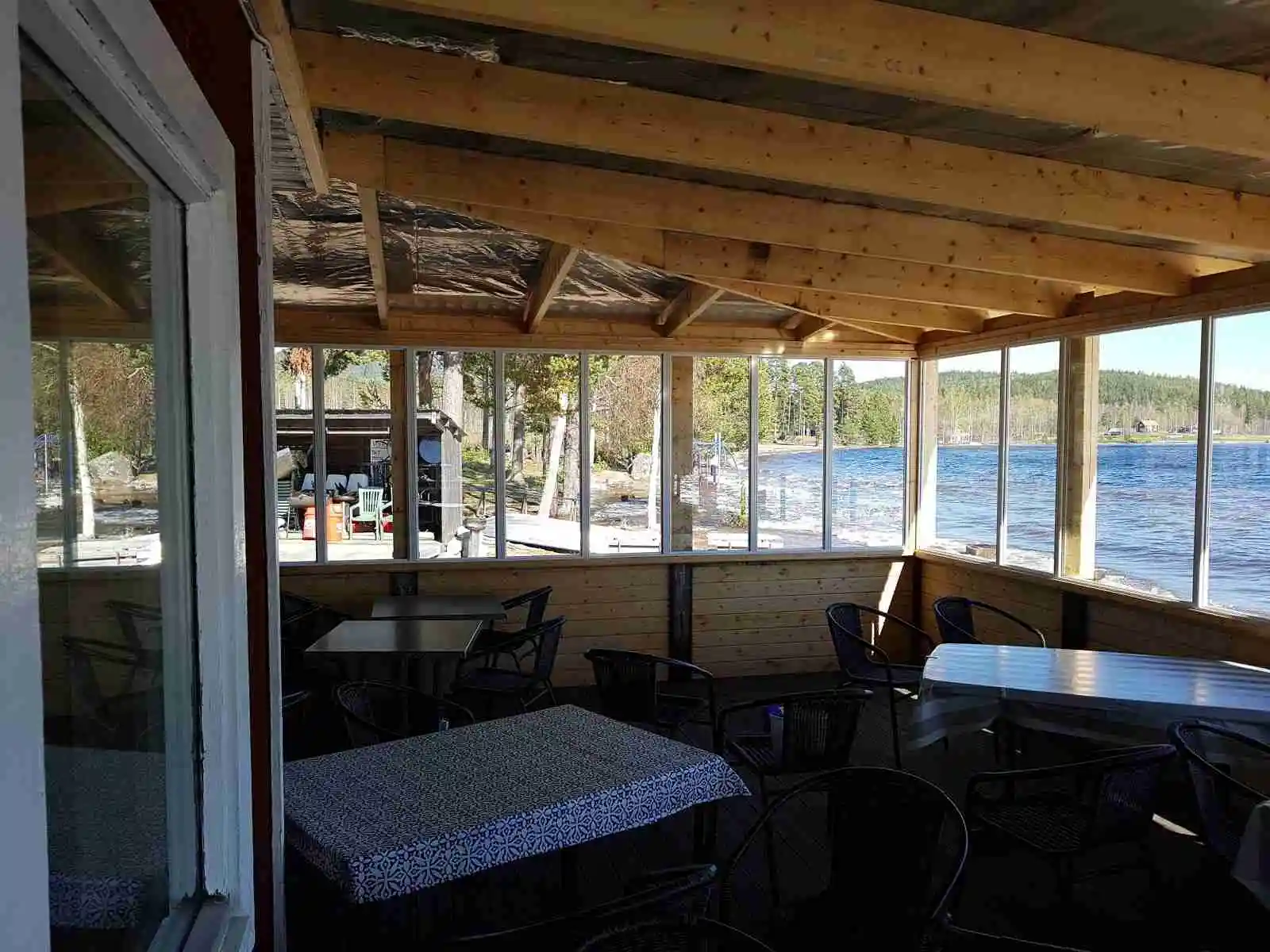 En träveranda med bord och stolar i skuggan, omgiven av skog. Ett perfekt ställe för att koppla av, vid Norra Dellen Familjecamping.