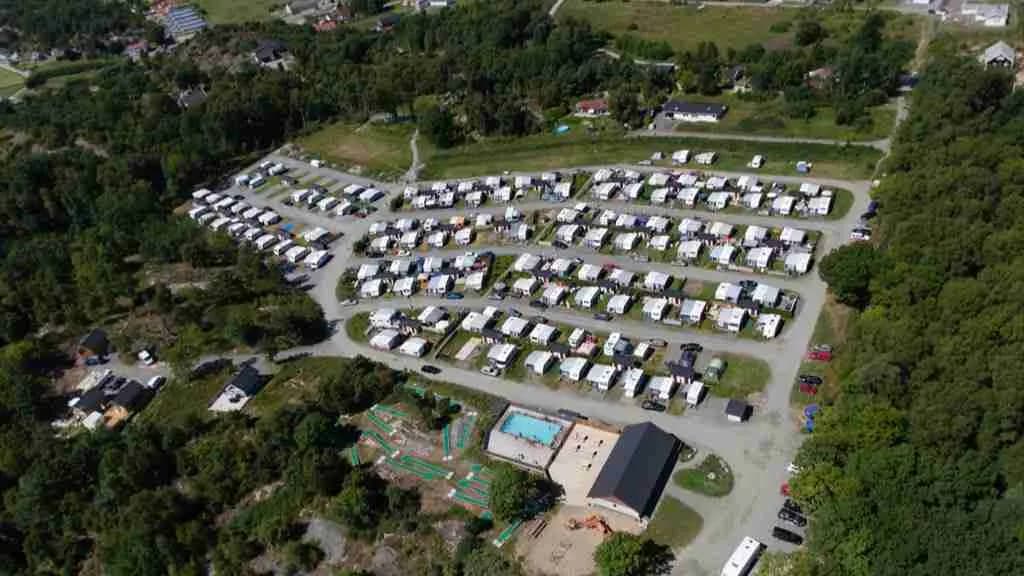 Flygfoto över Stråvalla Camping visar en anläggning med parkeringsplatser, husvagnar och gröna områden, omgiven av bostadsområden i förortsmiljö.