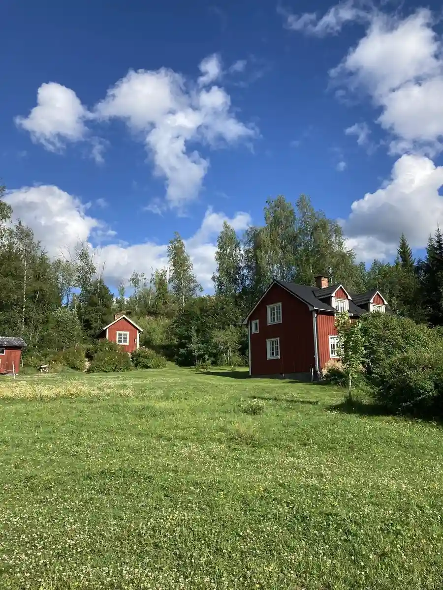 En lantlig gård omgiven av grönska med gräs och träd, med ett mysigt hus i mitten av ett stort, öppet landskap.