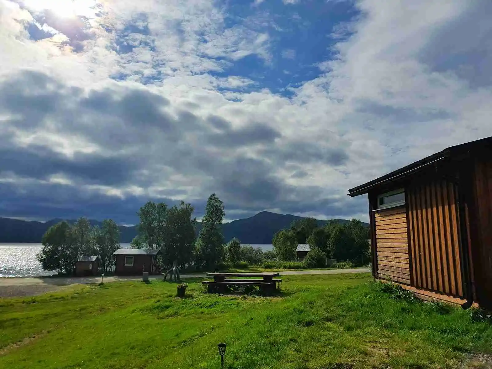 En vidsträckt äng under en molnig himmel, med ett enkelt skjul eller stuga belägen i den lantliga omgivningen vid Lia Ranch vildmarkscamping.