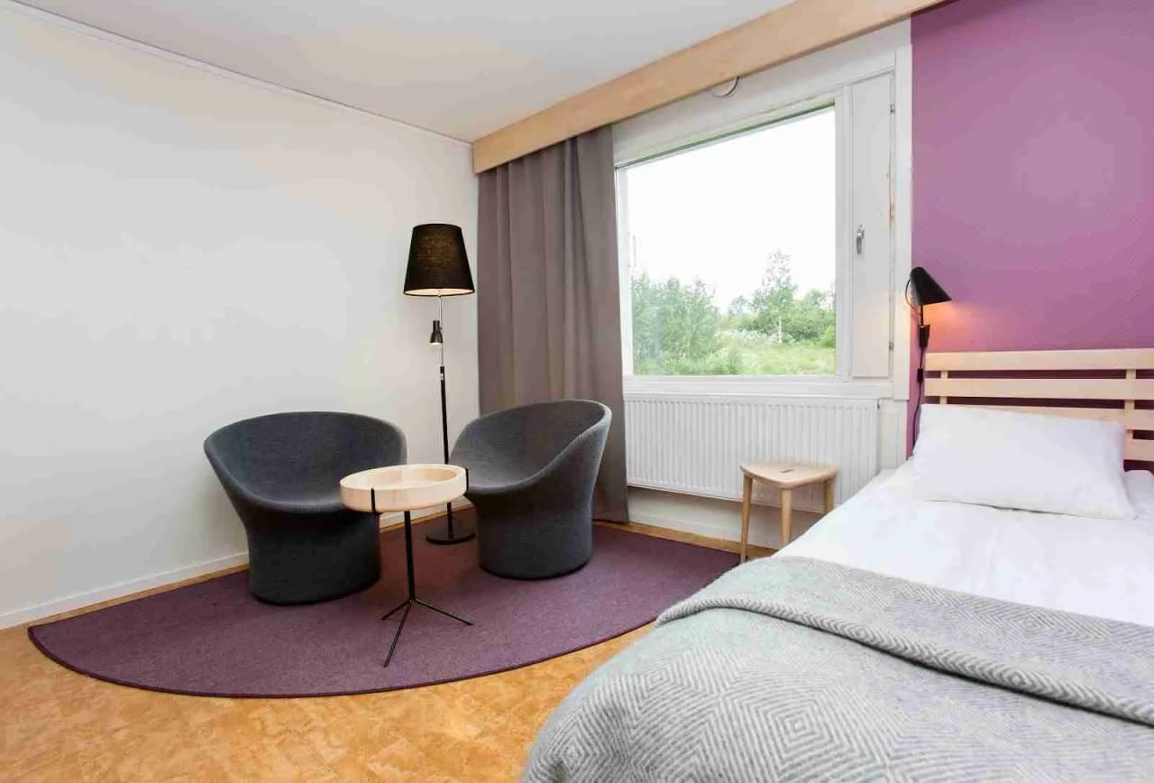 En mysig sovrumsmiljö på Camp Ripan med en bekväm dubbelsäng, moderna möbler och smakfullt inredd med ljusa färger. Taklampan ger ett varmt sken över det trägolvade rummet, vilket skapar en inbjudande och avkopplande atmosfär.