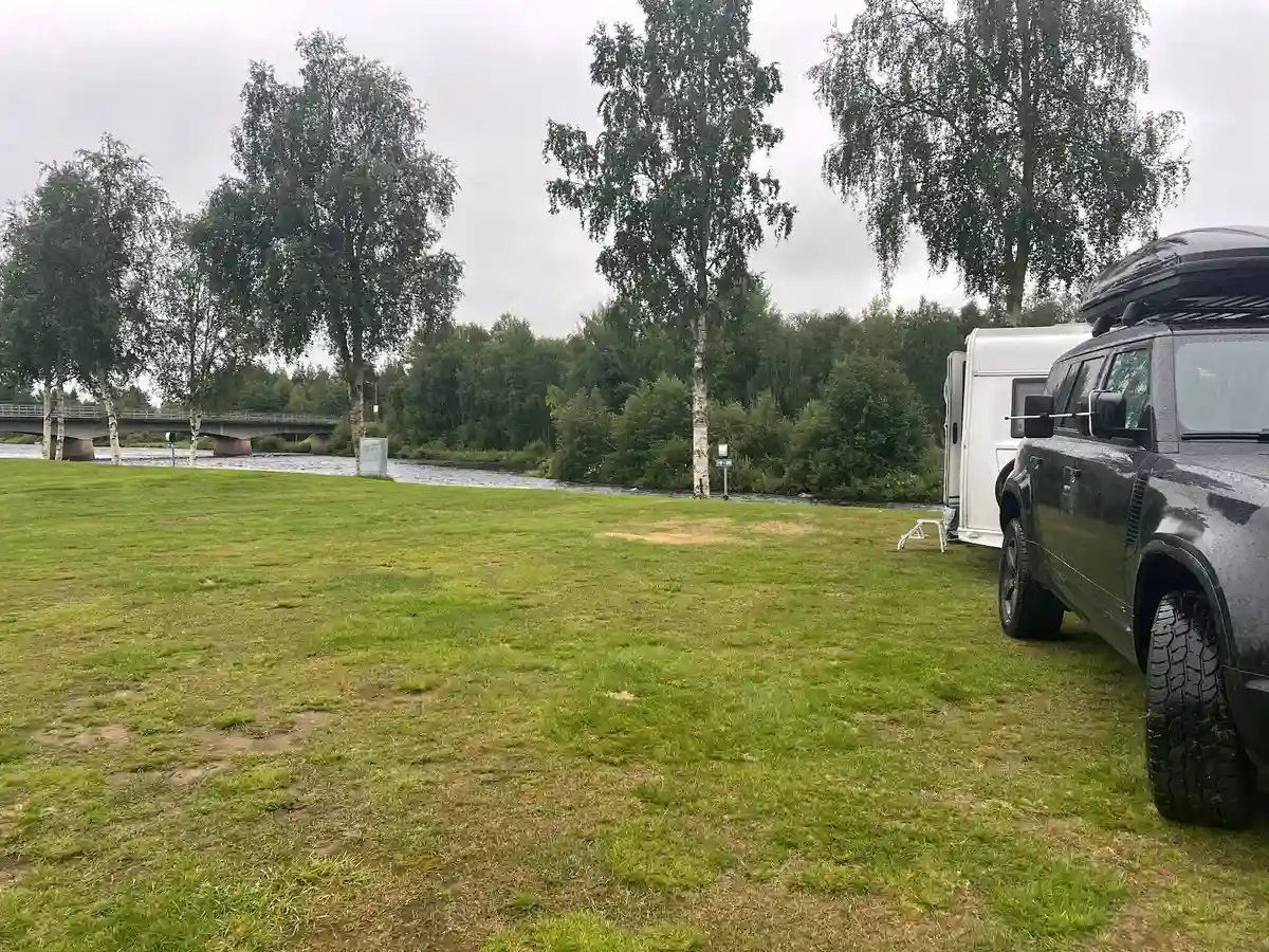 En bil parkerad på Lillhärdals camping, med ett lastgaller på taket. Omgivningen visar en campingmiljö med grönska.
