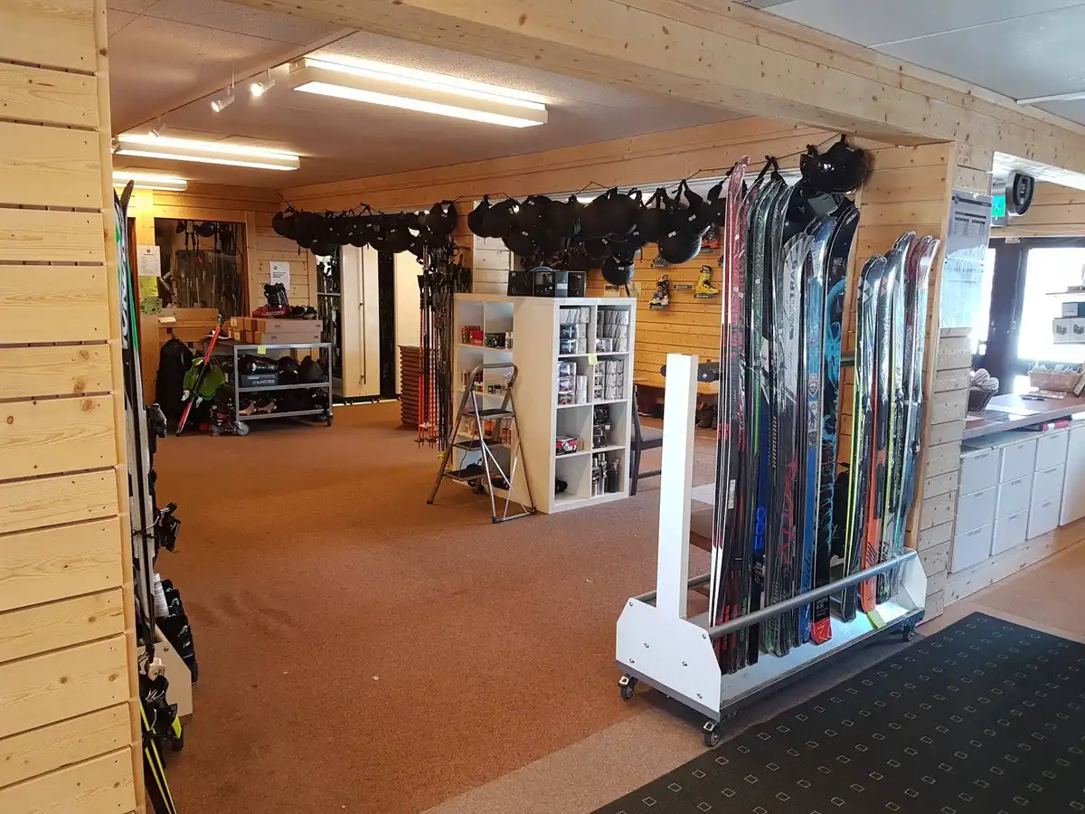 Inomhusmiljö i en sportbutik med skidutrustning uppställd på hyllor, inklusive skidor och skidstavar, med ett trätak och ljusarmaturer ovanför.