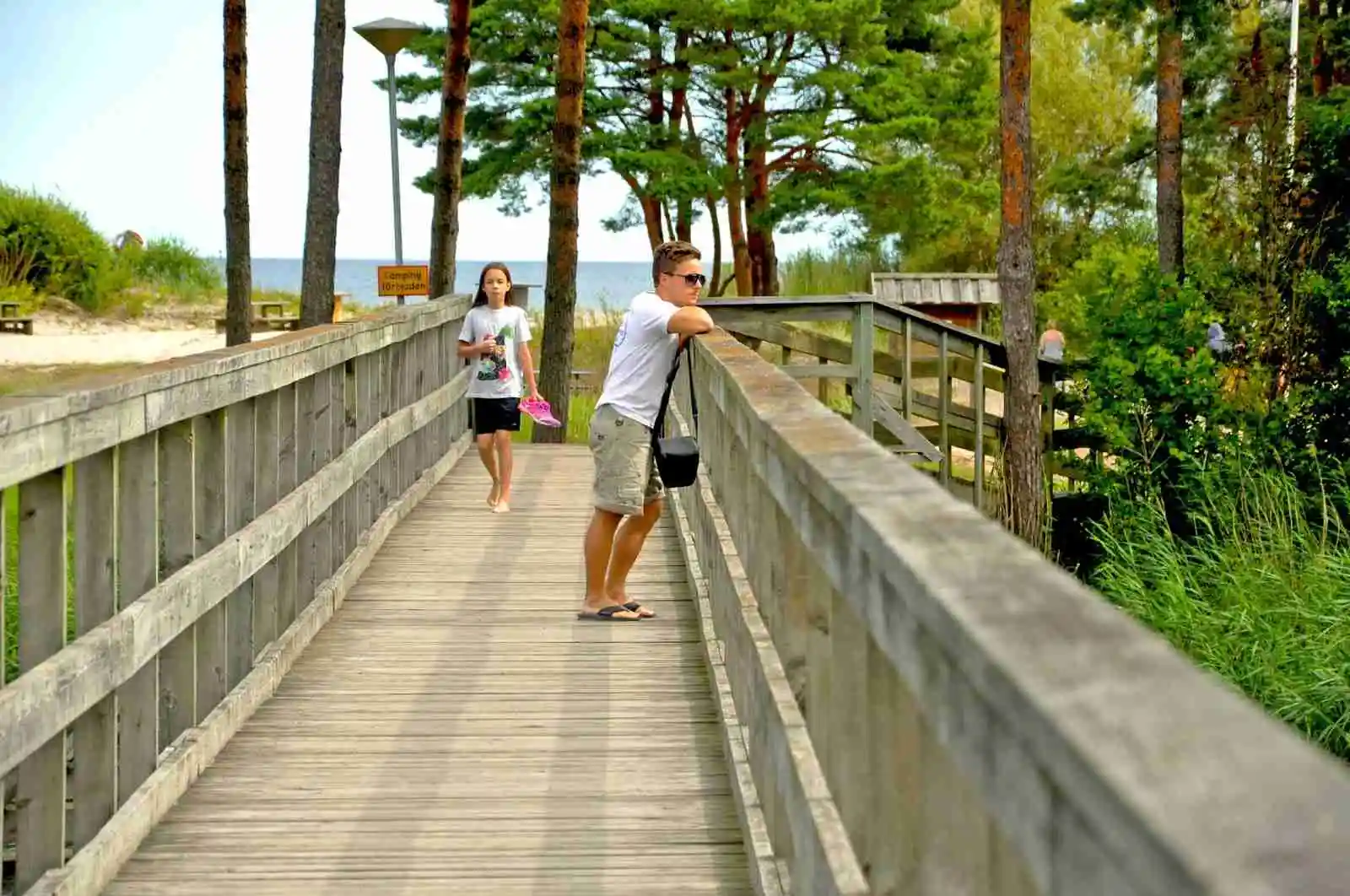 En träbrygga med ett staket som leder genom ett naturskönt område vid Åminne Fritid & Havsbad AB.