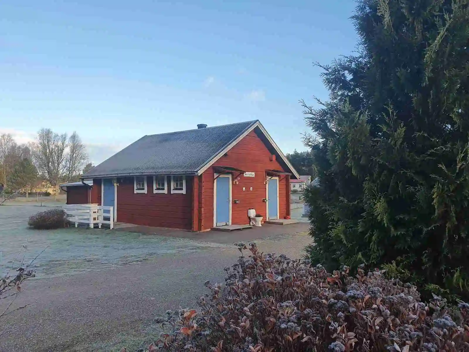 En stuga på Höljes camping med bilar parkerade framför. Stugans tak är väl synligt och området ger en hemtrevlig känsla.