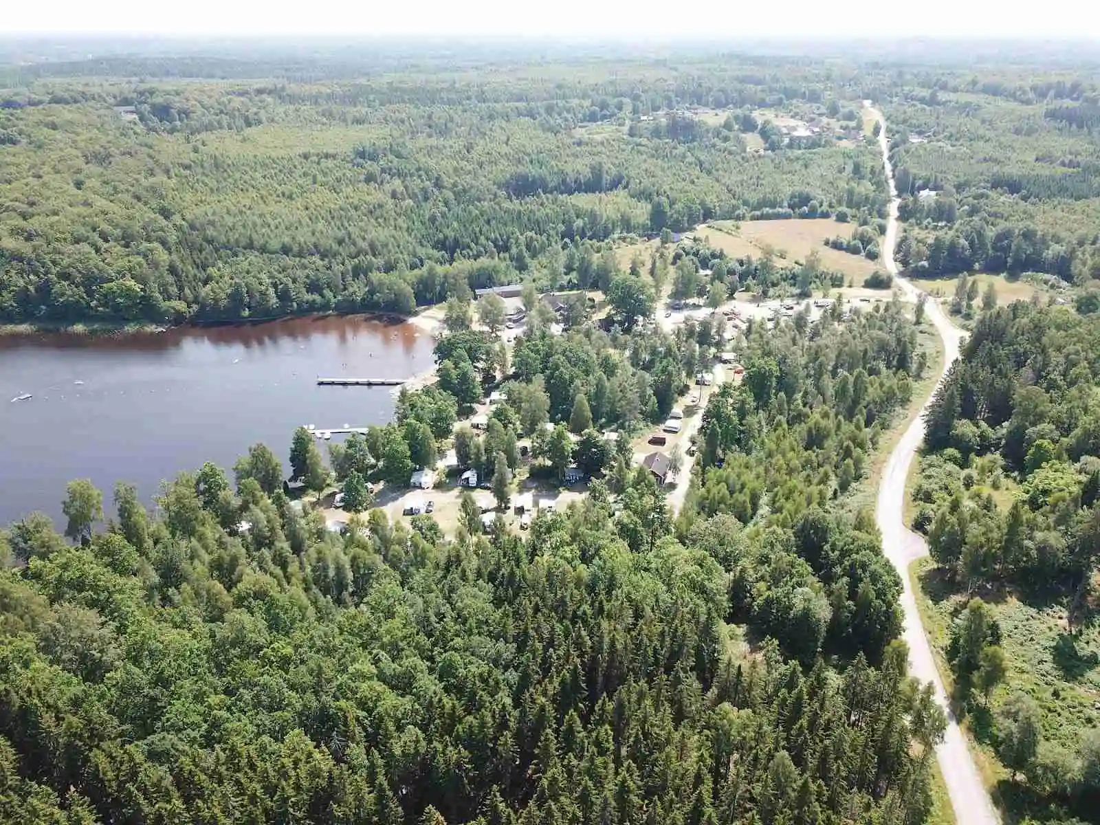 Flygfoto över Hätteboda Vildmarkscamping visar en frodig skogslandskap med en slingrande flod som rinner genom området. Träd täcker större delen av landskapet, vilket skapar en känsla av orörd natur och avskildhet.