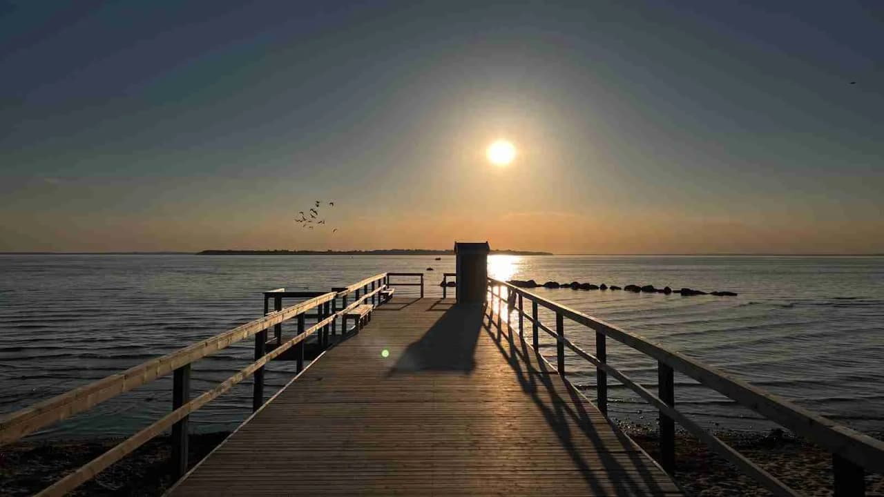 En solnedgång över havet vid Borstahusen, med en brygga som sträcker sig ut i vattnet och en klar himmel i bakgrunden.