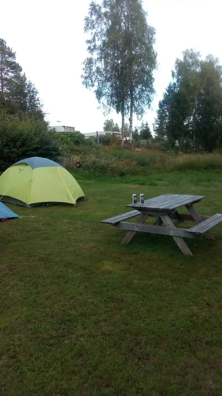 En tältplats på Norrmjöle camping med ett tält och en picknickbord under en molnig himmel, omgiven av en grön gräsyta.