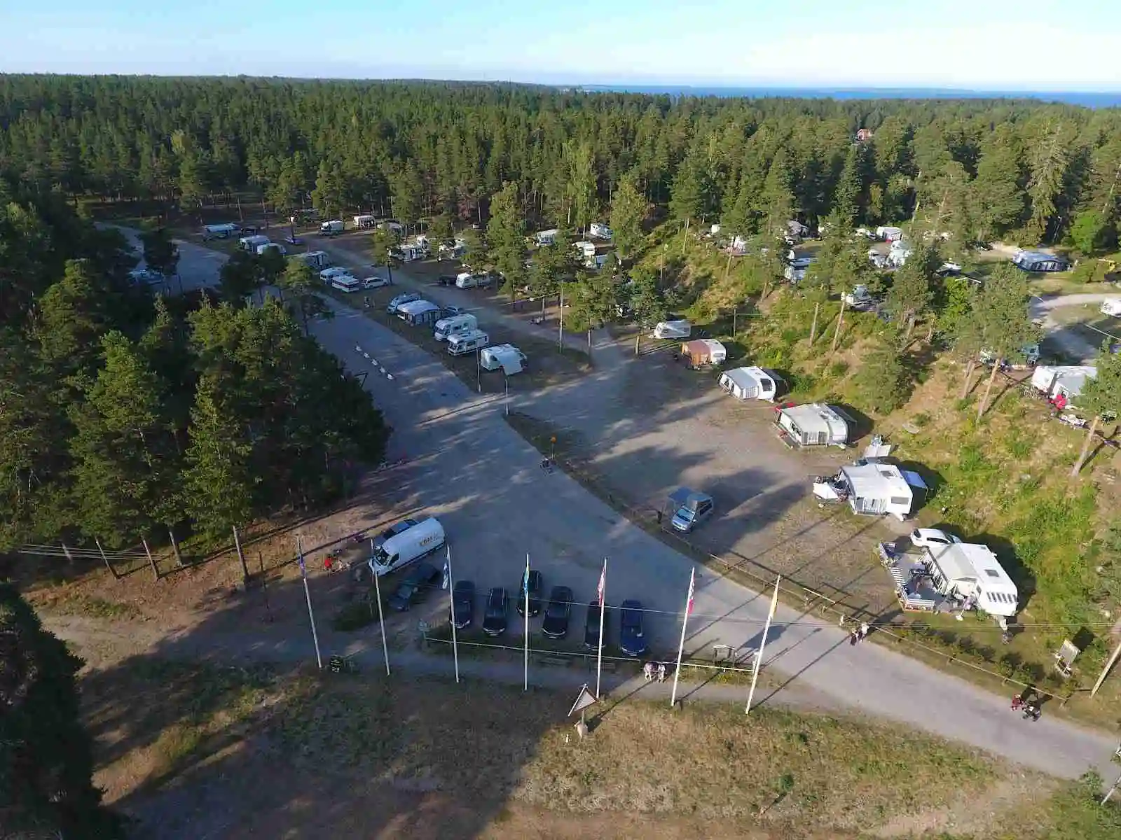 Bild av Gävle Camping Engesberg från ovan, visar en parkeringsplats med husbilar, lastbilar och campingvagnar i en naturskön miljö.