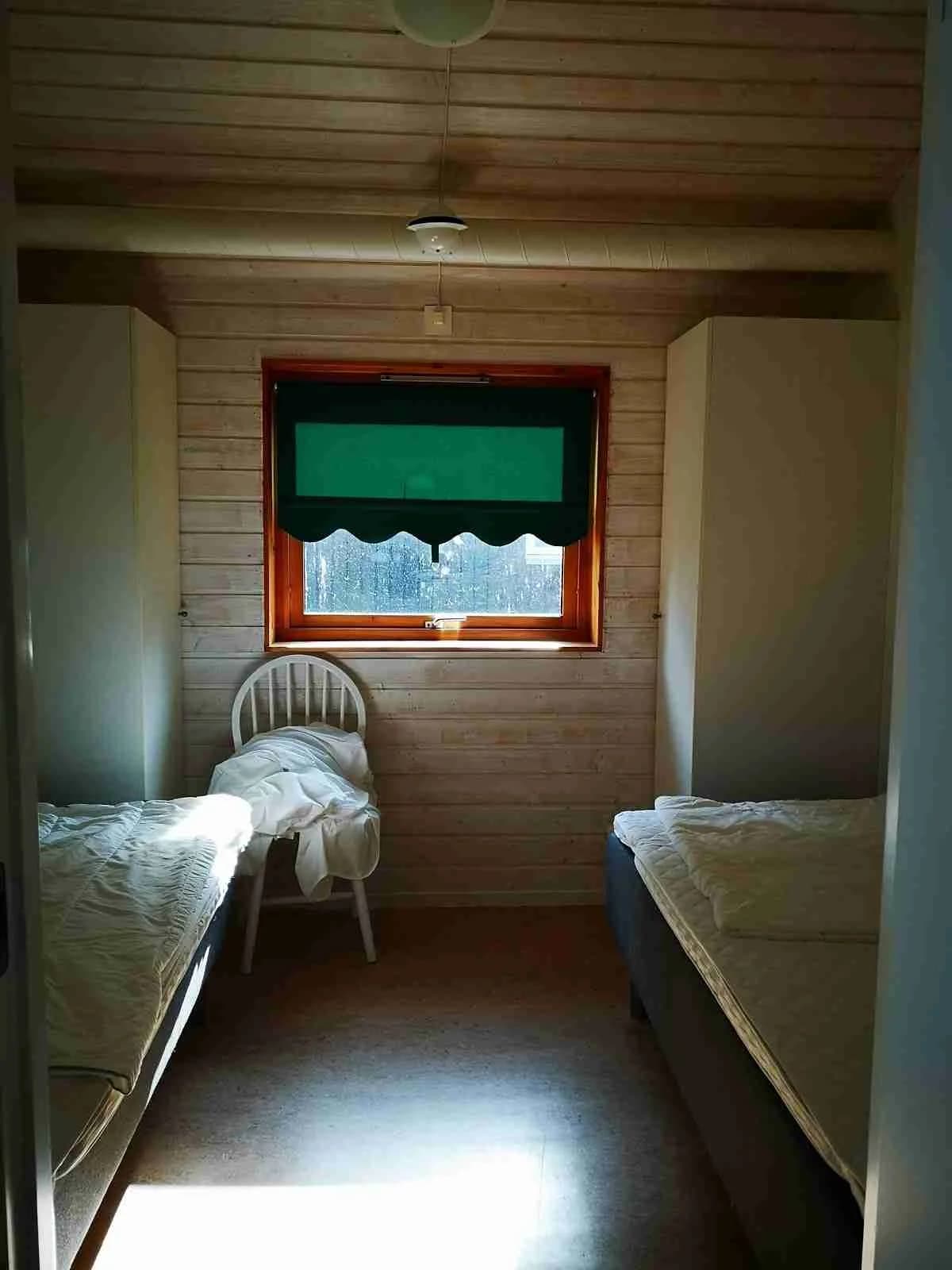 Ett mysigt sovrum med träinredning, där ett bekvämt täckt sängstativ är i fokus, omgiven av ett trägolv och träpaneler som ger en varm och inbjudande atmosfär.