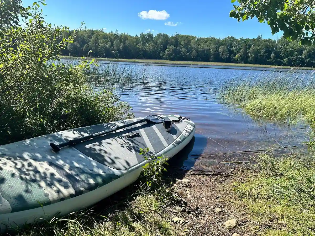 En lugn sjö med grönskande växtlighet runt omkring, där en kanot ligger förankrad vid strandkanten i vildmarkscampingen Hallsjö.