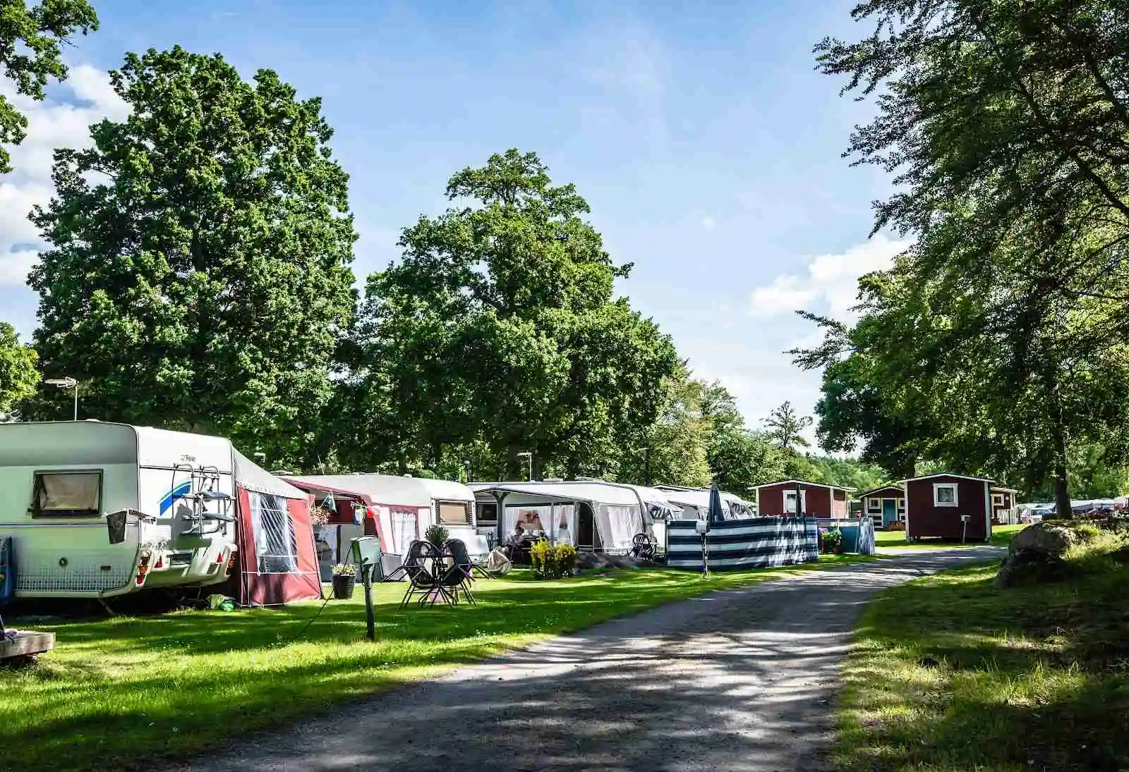 En campingplats med husvagnar och husbilar parkerade på en grön gräsmatta omgiven av träd.