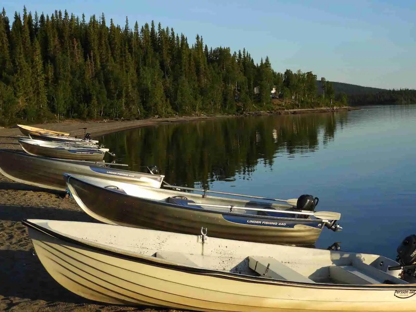 En kanot ligger vid strandkanten av en sjö, omgiven av lugn vildmark och klart vatten.