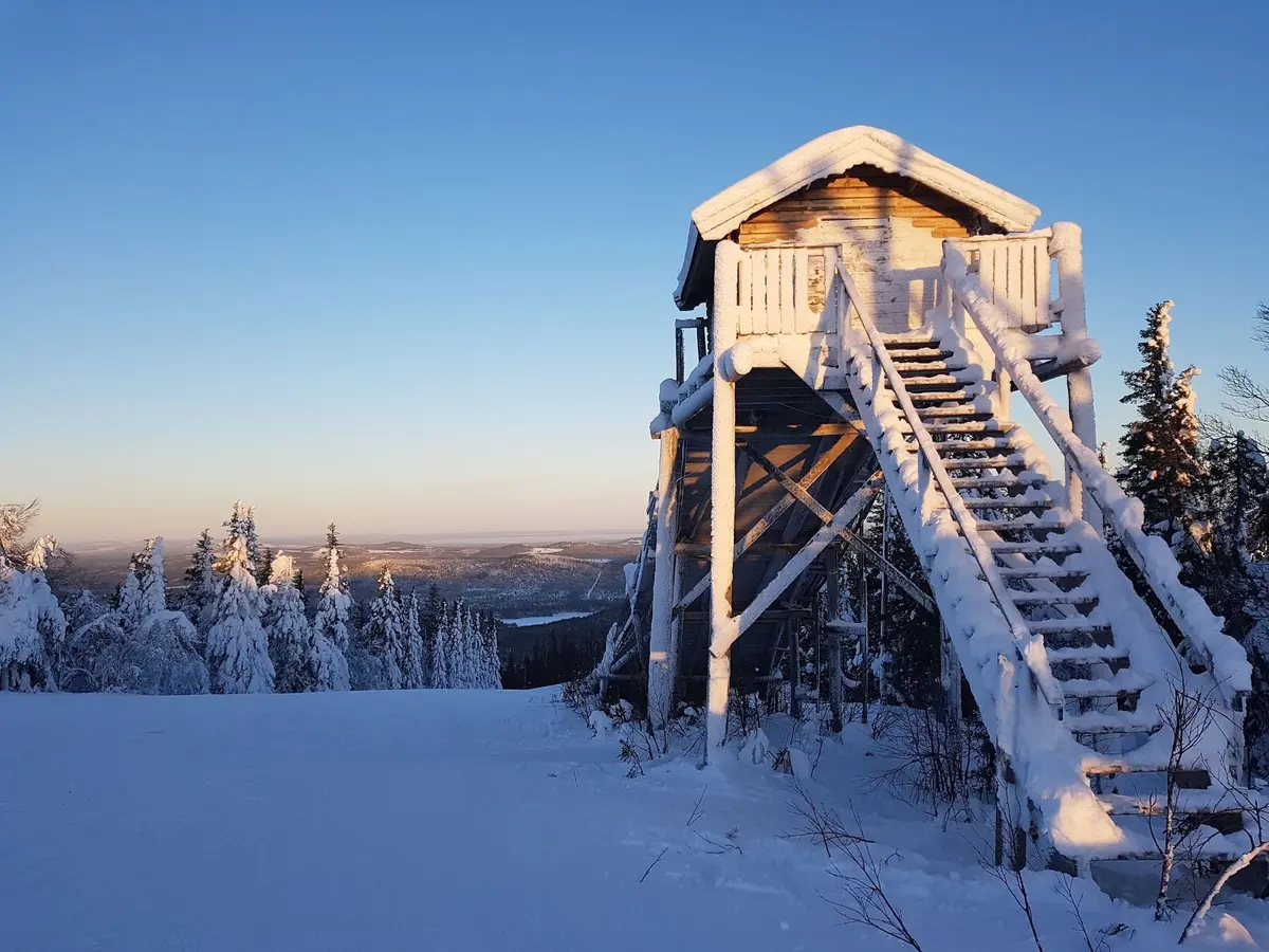 En snöklädd stuga vid foten av en vintrig skidbacke, omgiven av ett fruset landskap.